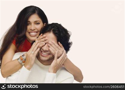 Portrait of a young woman covering eyes of a young man from behind