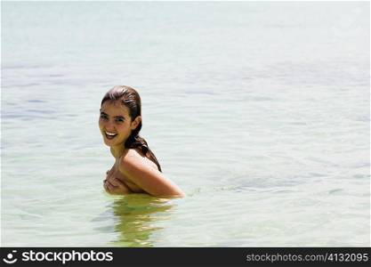 Portrait of a young woman covering her breast with her hands and smiling in the sea