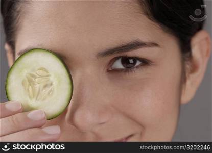Portrait of a young woman covering her eye with a cucumber slice