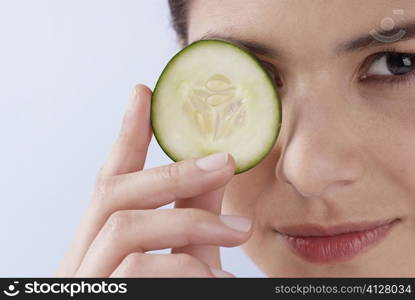 Portrait of a young woman covering her eye with a cucumber slice