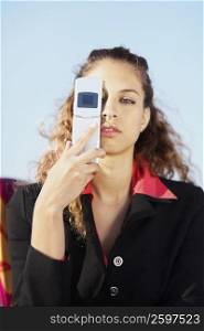 Portrait of a young woman covering her eye with a mobile phone