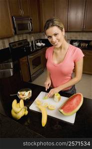 Portrait of a young woman cutting fruits on a cutting board and smiling