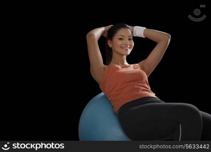 Portrait of a young woman doing abdominal exercise on a fitness ball over black background