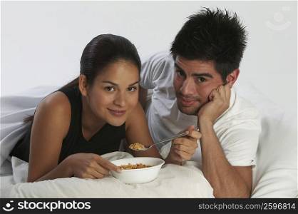 Portrait of a young woman eating a bowl of cereals with a young man beside her