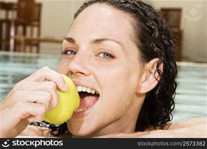 Portrait of a young woman eating a green apple in a swimming pool