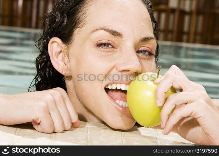 Portrait of a young woman eating a green apple in a swimming pool