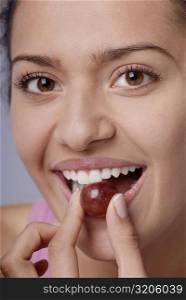 Portrait of a young woman eating a red grape