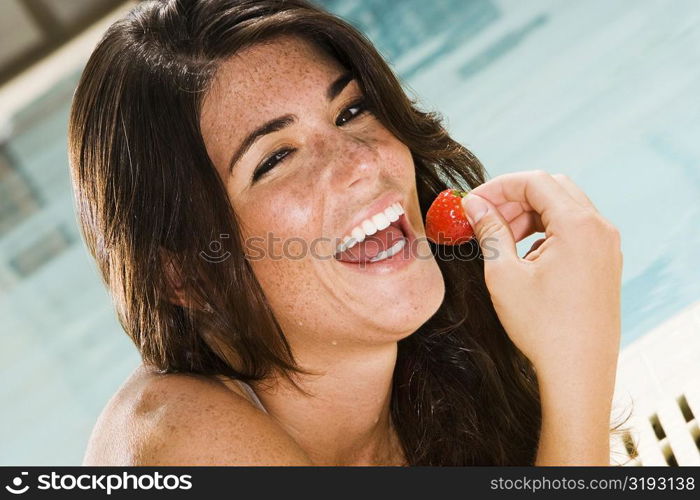 Portrait of a young woman eating a strawberry at the poolside