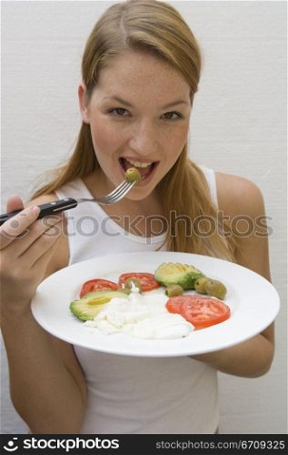 Portrait of a young woman eating an olive with a fork