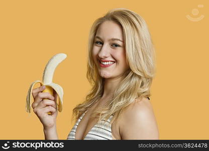 Portrait of a young woman eating banana over colored background