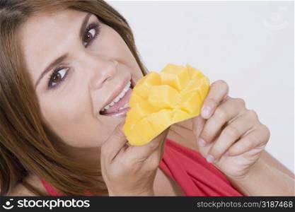 Portrait of a young woman eating cubes of a mango and smiling