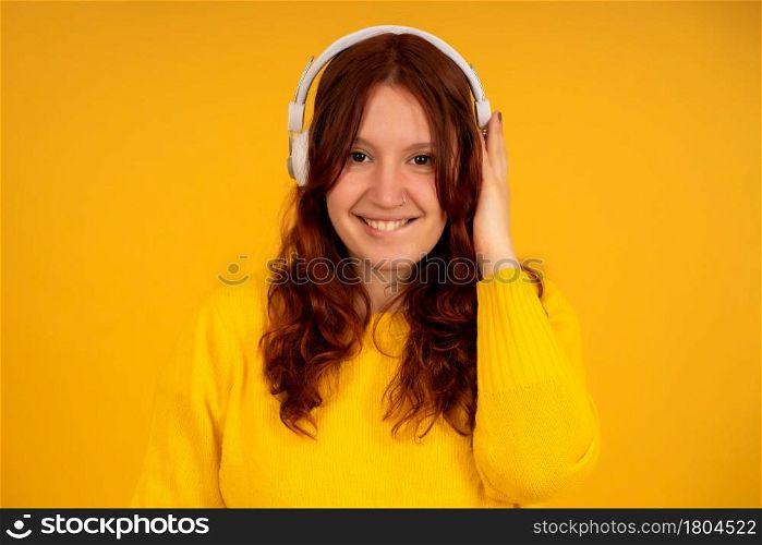 Portrait of a young woman enjoying listening to music with headphones while standing against isolated yellow background.