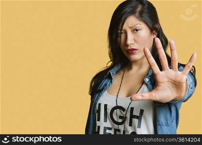 Portrait of a young woman gesturing stop sign over colored background