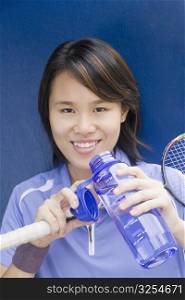 Portrait of a young woman holding a badminton racket and a water bottle