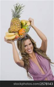 Portrait of a young woman holding a basket of assorted fruits and smiling