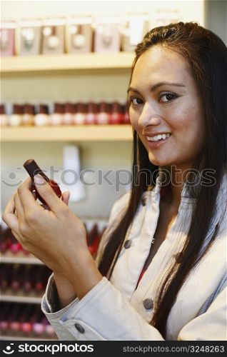 Portrait of a young woman holding a bottle of nail polish and smiling