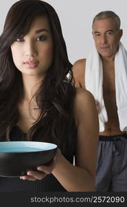 Portrait of a young woman holding a bowl and her father standing behind her