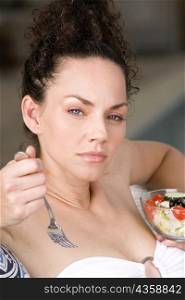 Portrait of a young woman holding a bowl of fruit salad and a fork