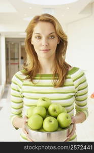 Portrait of a young woman holding a bowl of green apples