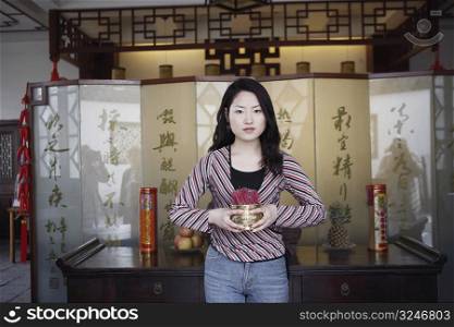 Portrait of a young woman holding a bowl of incense sticks