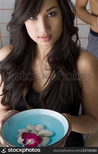Portrait of a young woman holding a bowl of water with stones and a rose