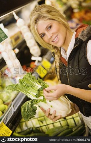 Portrait of a young woman holding a Chinese cabbage in a supermarket