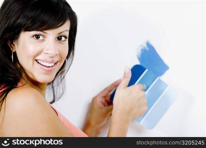 Portrait of a young woman holding a color swatch against a wall