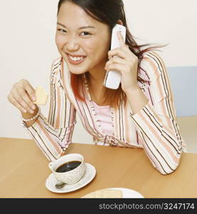 Portrait of a young woman holding a cookie and talking on a mobile phone