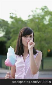 Portrait of a young woman holding a cotton candy and sucking her thumb