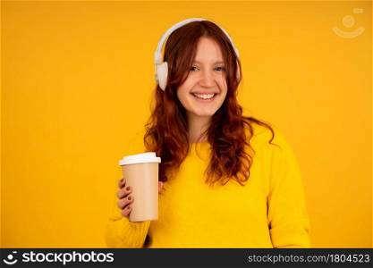 Portrait of a young woman holding a cup of coffee while enjoying listening to music with headphones against isolated background.