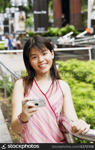 Portrait of a young woman holding a digital camera and smiling