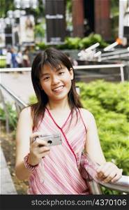 Portrait of a young woman holding a digital camera and smiling