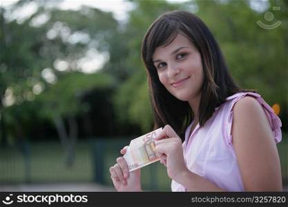 Portrait of a young woman holding a fifty Euro banknote and smiling