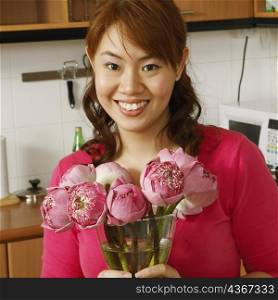 Portrait of a young woman holding a flower vase in the kitchen