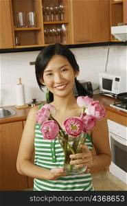 Portrait of a young woman holding a flower vase in the kitchen