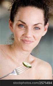 Portrait of a young woman holding a fork with a cucumber slice