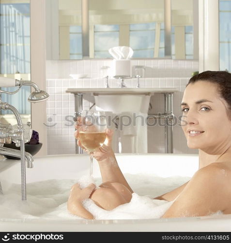 Portrait of a young woman holding a glass of a wine in a bathtub