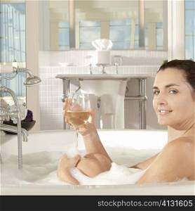 Portrait of a young woman holding a glass of a wine in a bathtub