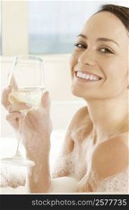 Portrait of a young woman holding a glass of white wine in the bathtub