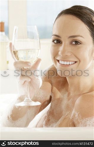 Portrait of a young woman holding a glass of white wine in the bathtub
