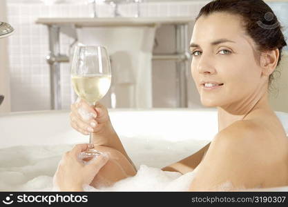 Portrait of a young woman holding a glass of wine in a bathtub