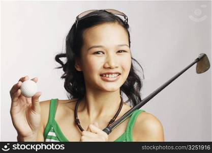 Portrait of a young woman holding a golf club and a golf ball