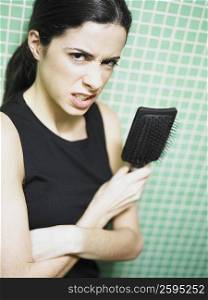 Portrait of a young woman holding a hair brush and grimacing