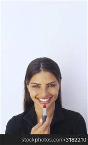 Portrait of a young woman holding a lipstick to her lips