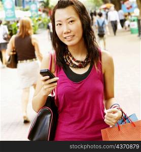 Portrait of a young woman holding a mobile phone and carrying shopping bags