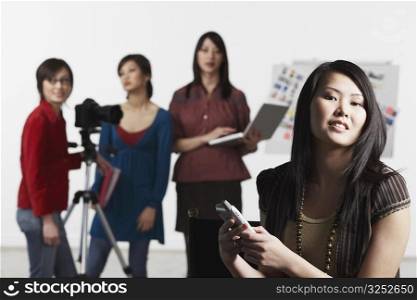 Portrait of a young woman holding a mobile phone with her friends standing behind her