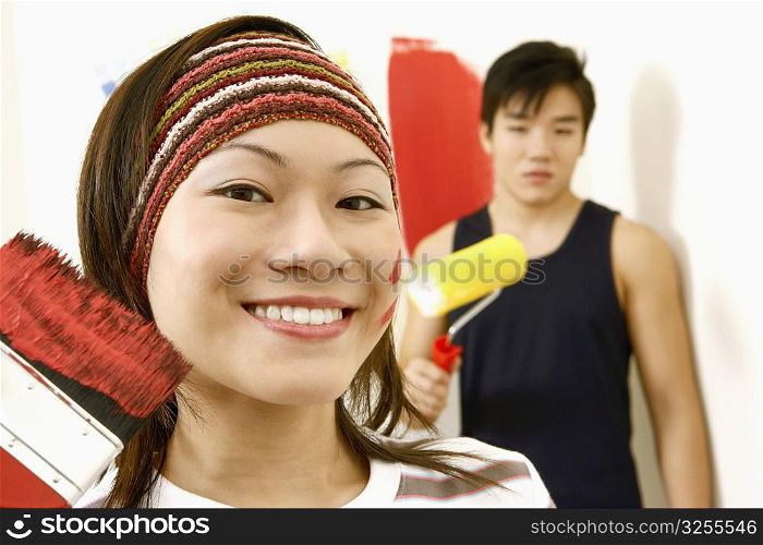 Portrait of a young woman holding a paint brush and a young man standing in the background