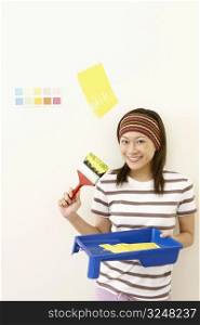 Portrait of a young woman holding a paint tray with a paintbrush and smiling