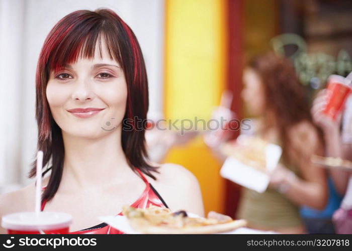 Portrait of a young woman holding a plate with a cold drink and a slice of pizza