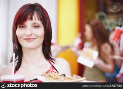 Portrait of a young woman holding a plate with a cold drink and a slice of pizza